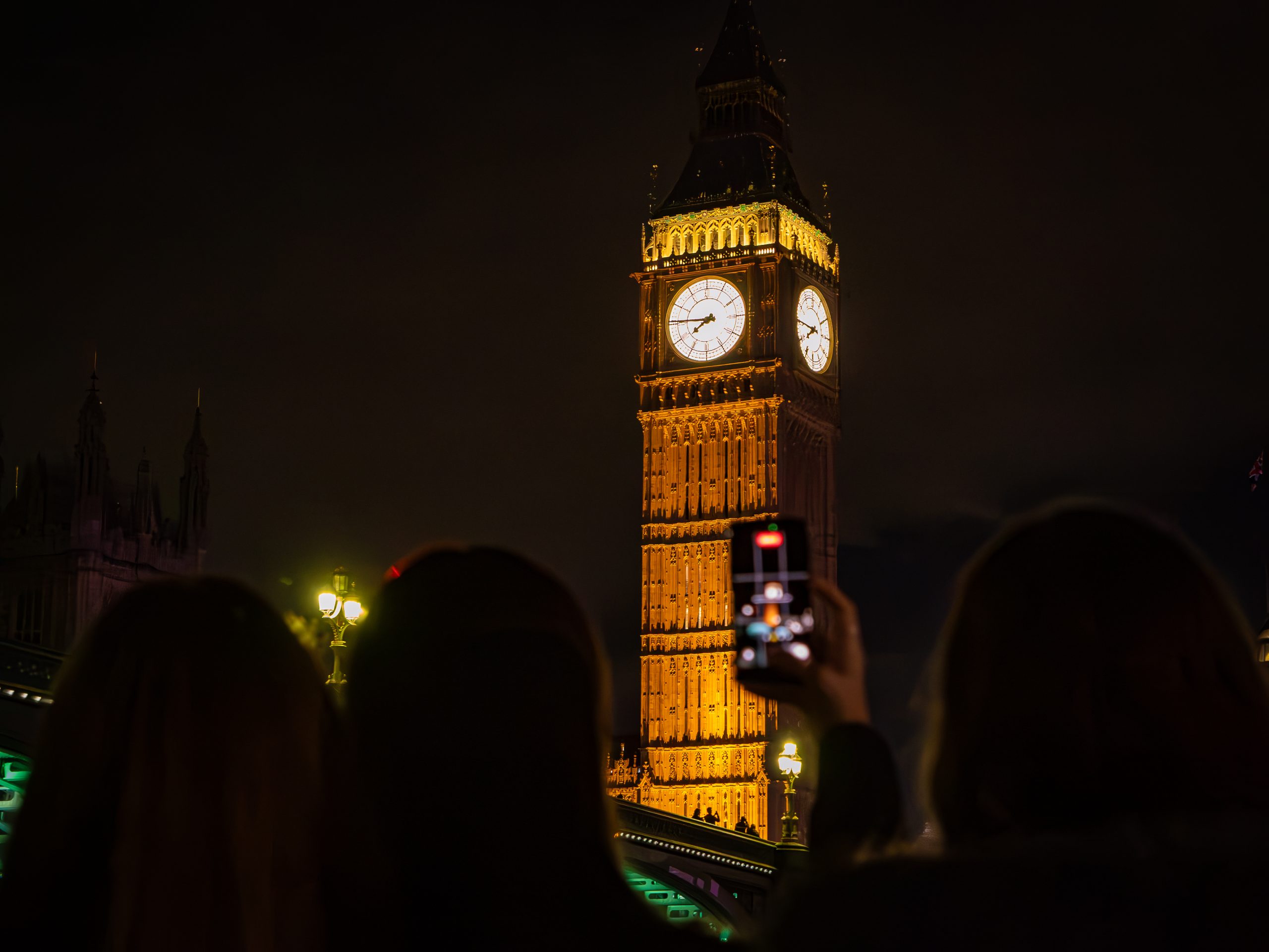 Silhouettes photographing illuminated Big Ben at night.