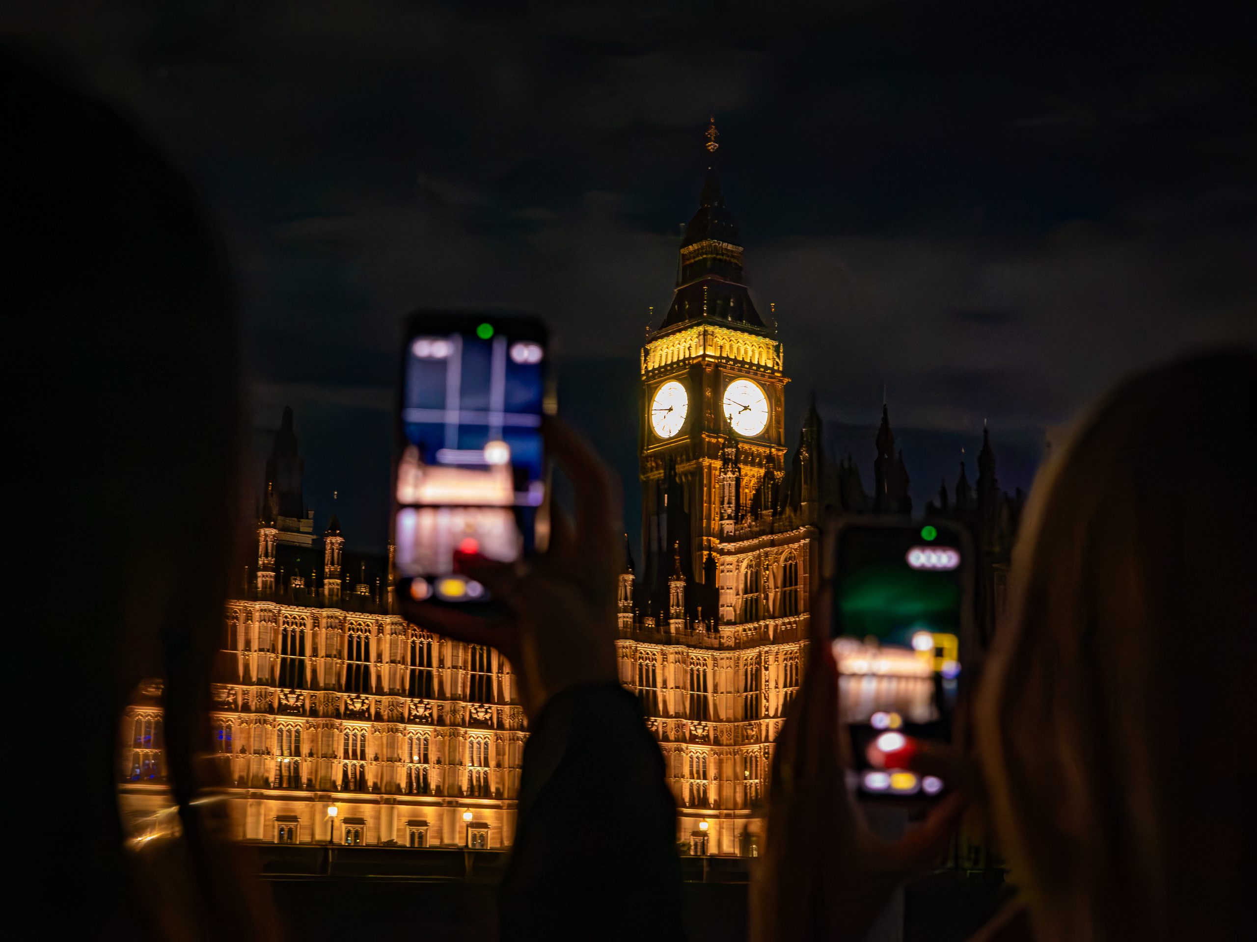 People taking photos of Big Ben at night with smartphones.