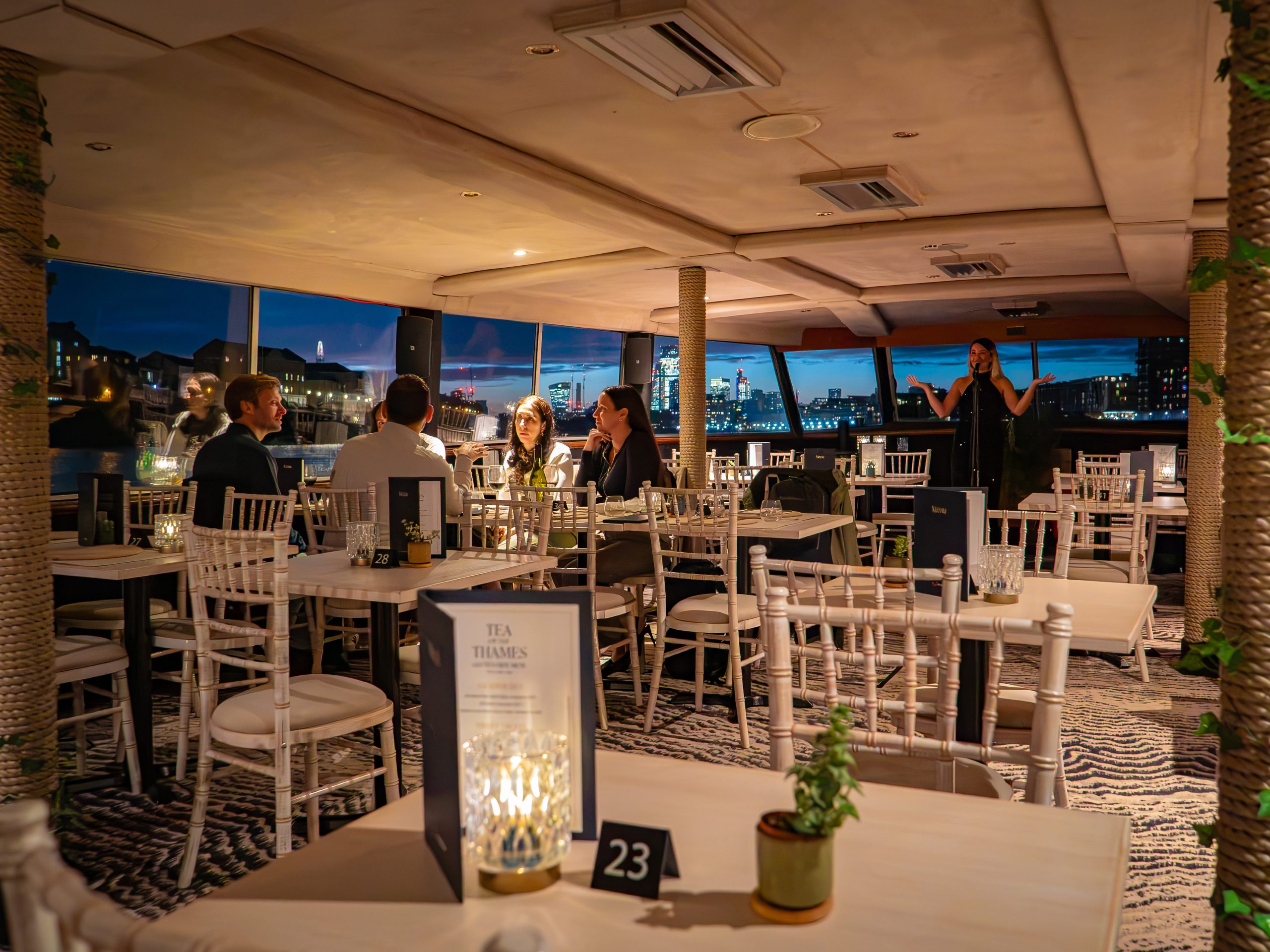 People dining in a cozy, dimly lit restaurant with large windows and city skyline view.
