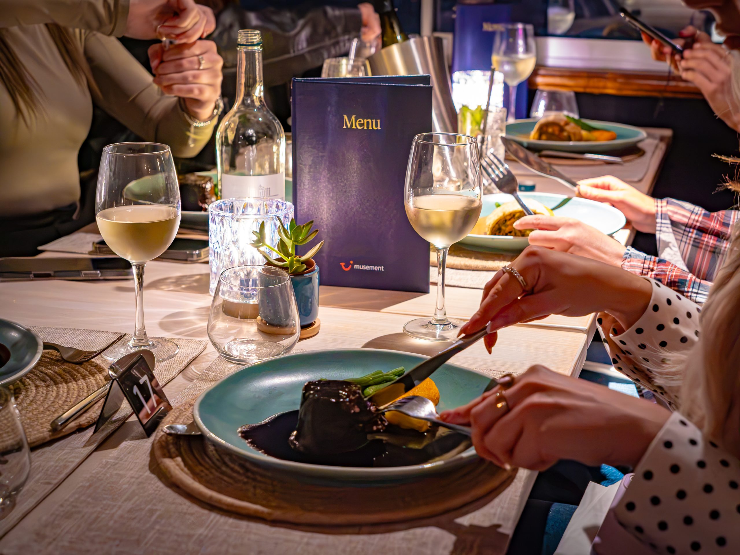 People dining at a table with wine, candles, and plates of food.