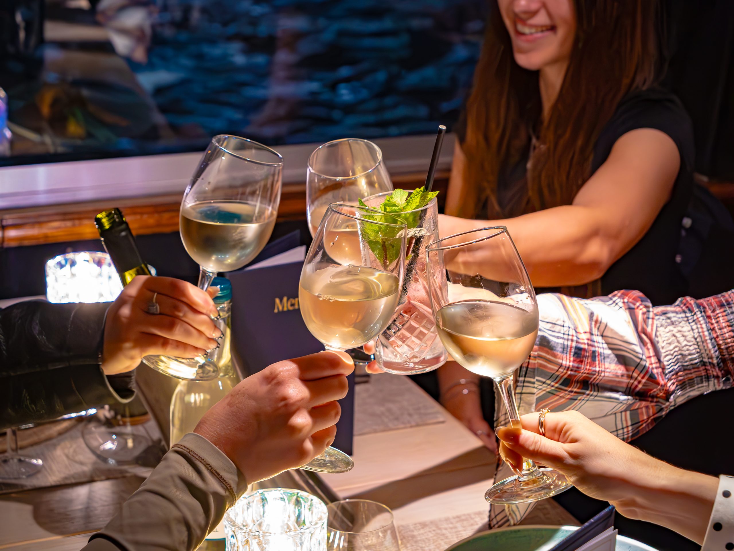 Group of people toasting with white wine glasses at a dinner table.