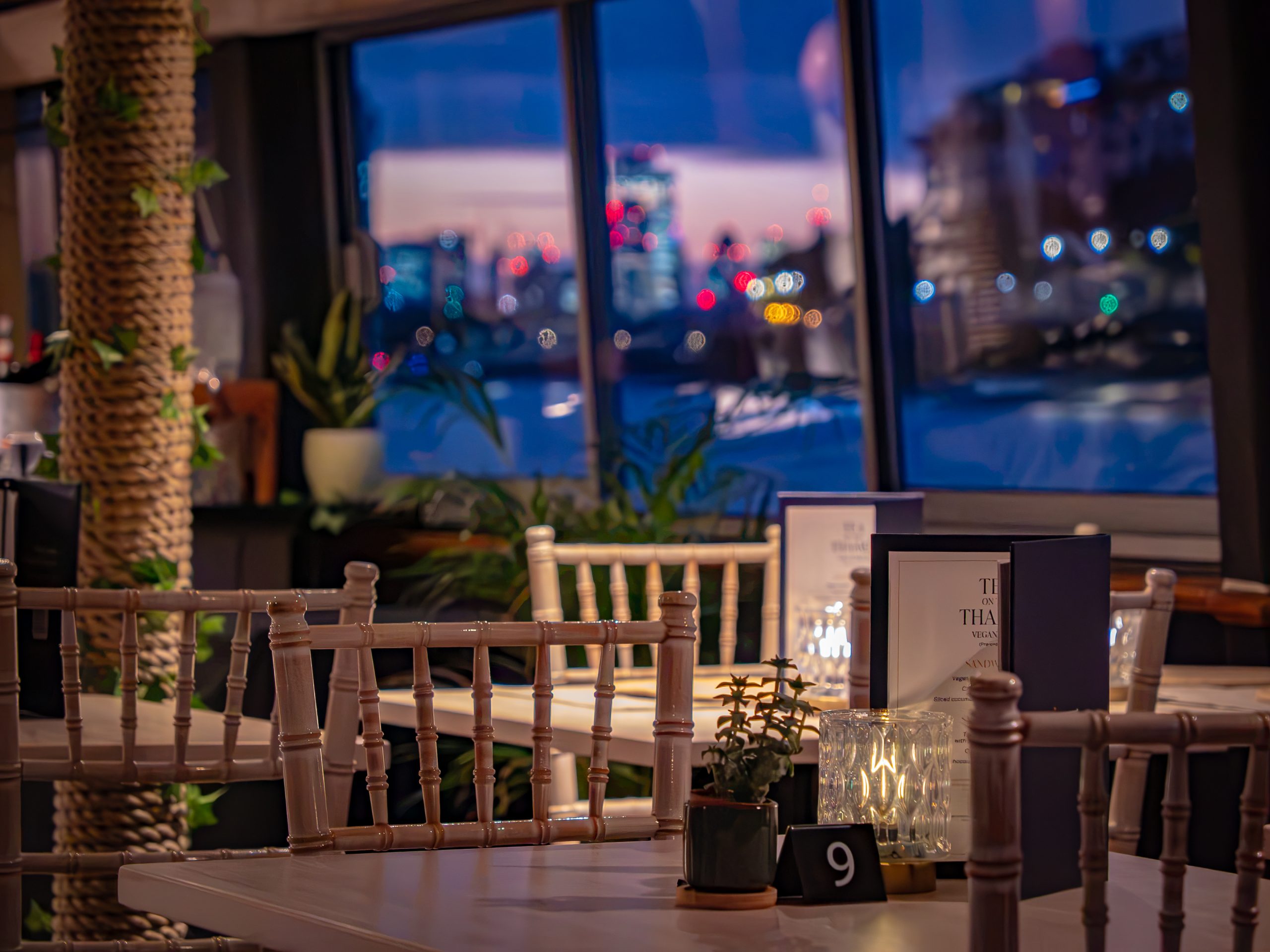 Cozy restaurant with cityscape view through large windows at dusk.