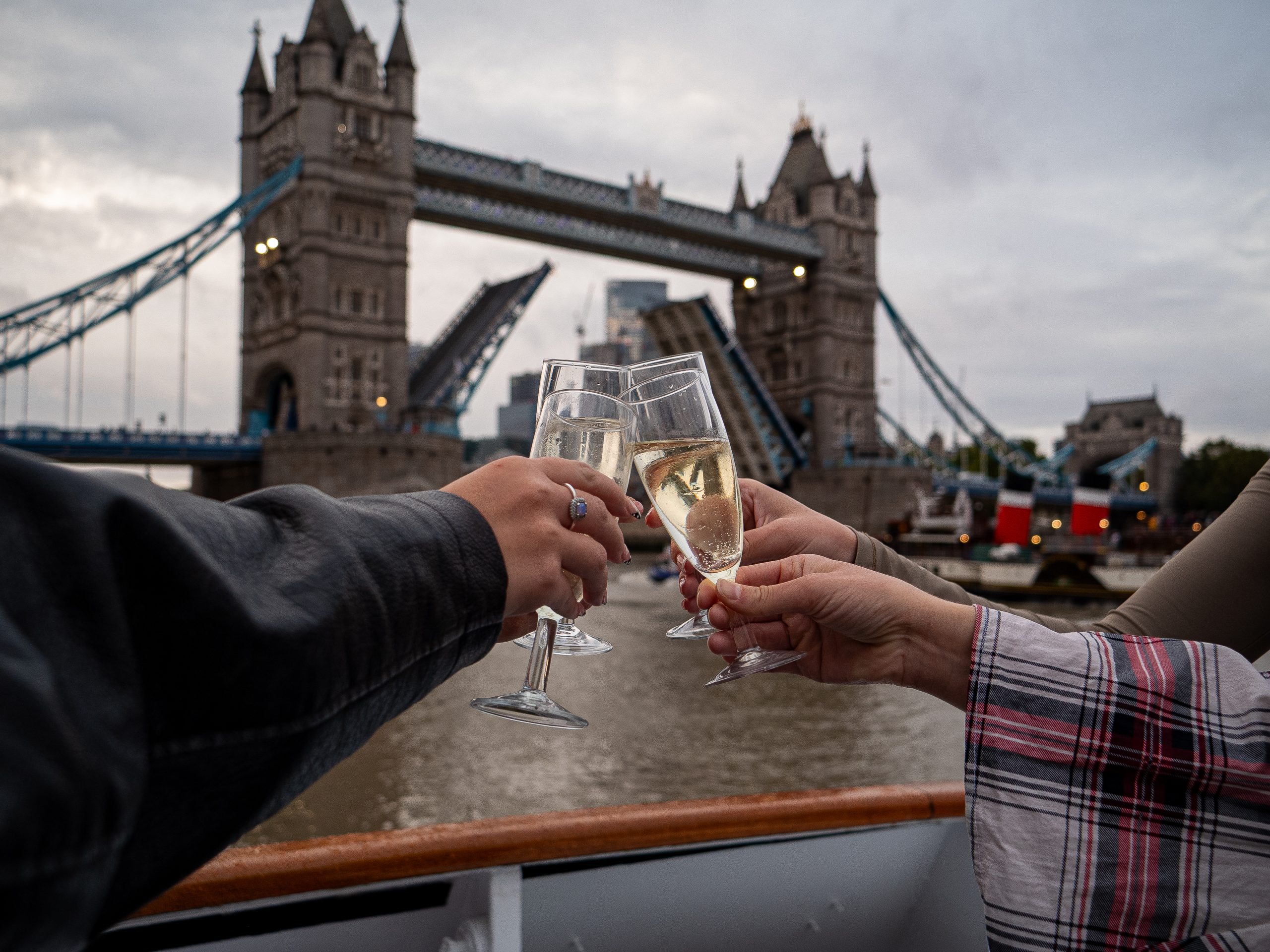 Hands toasting with champagne near Tower Bridge in London.
