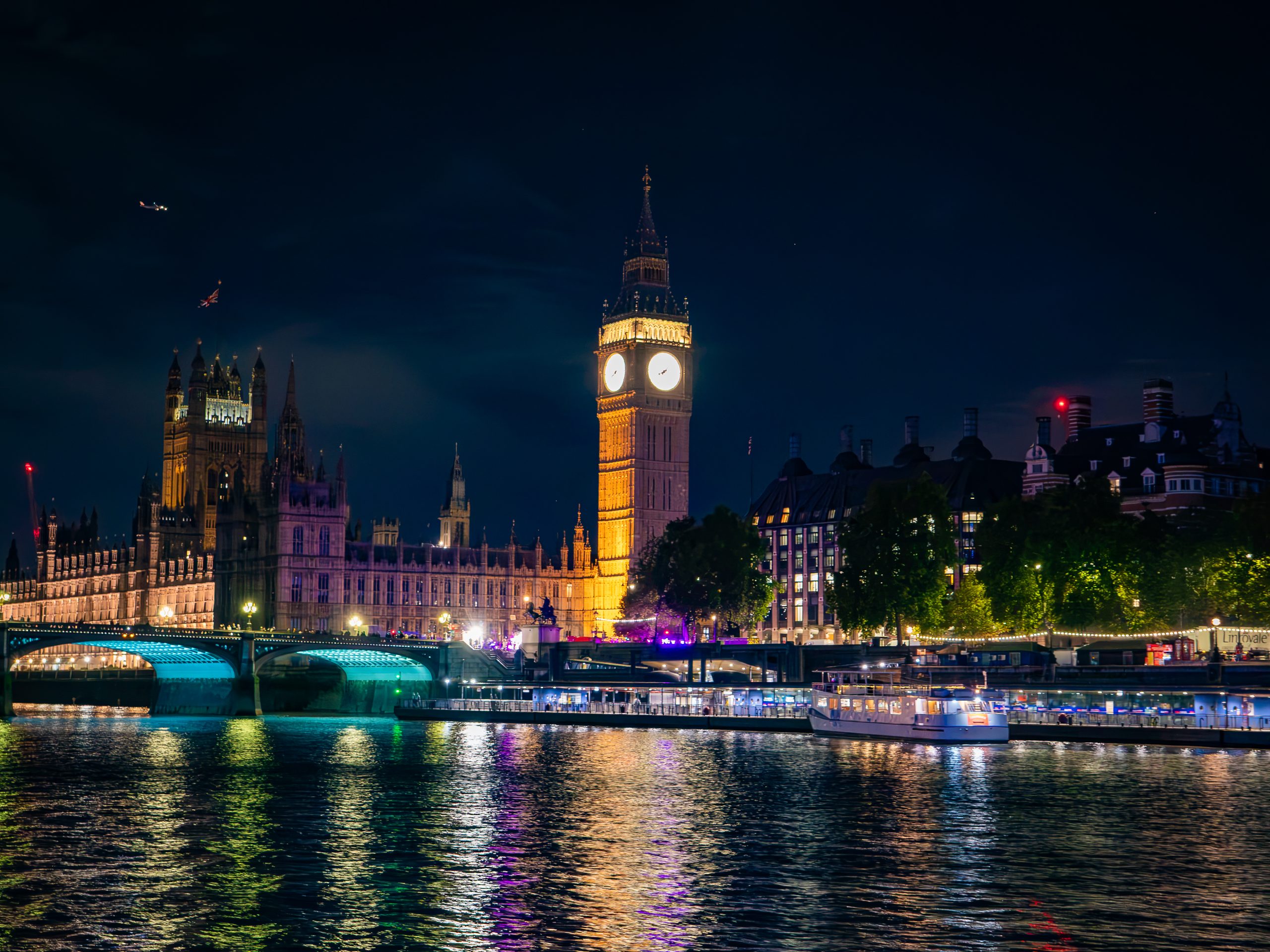 Night view of Big Ben and Thames River with illuminated bridge and buildings.