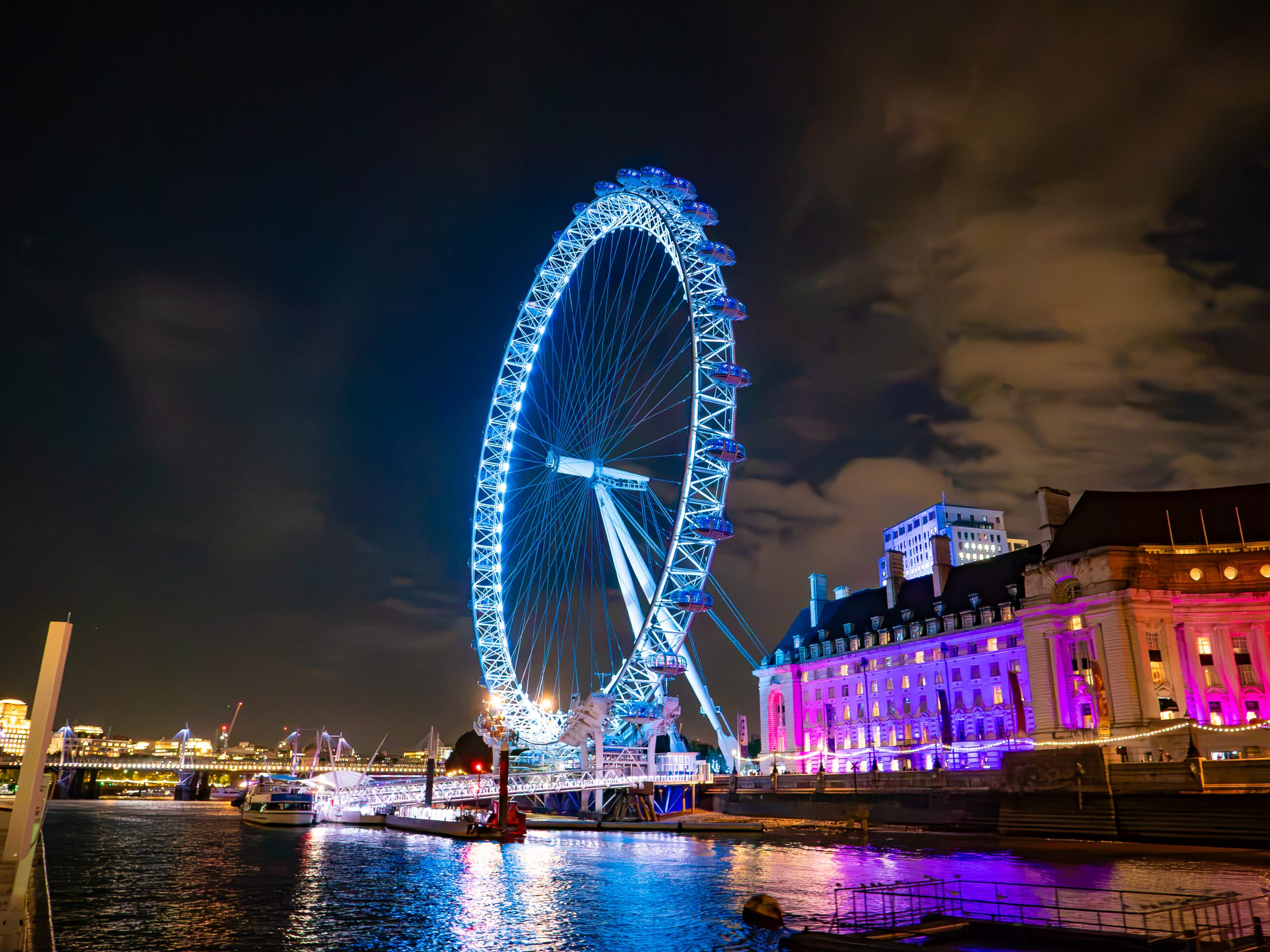 Illuminated Ferris wheel at night by a river with city lights.