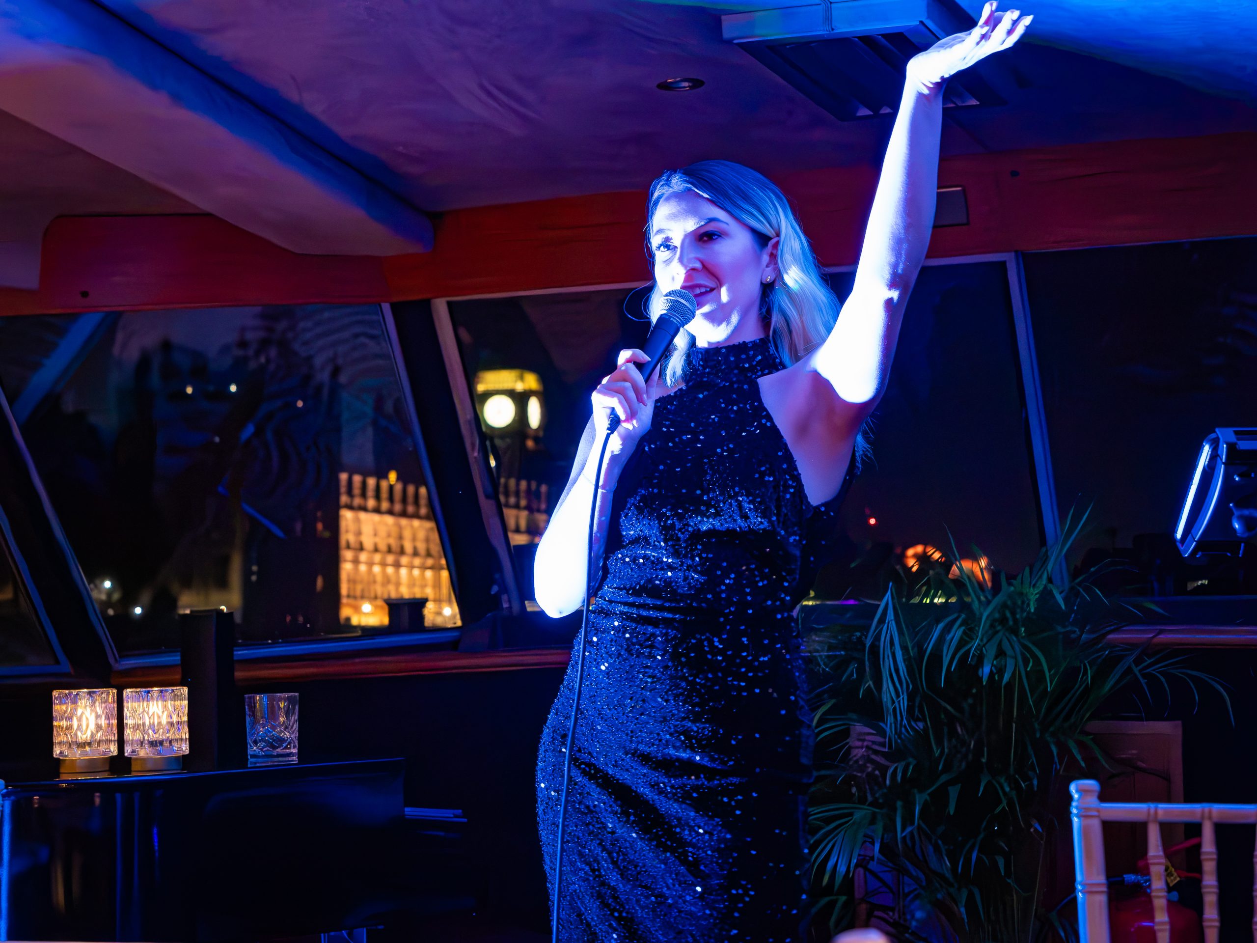 Woman in a black dress sings on stage with a microphone at night.