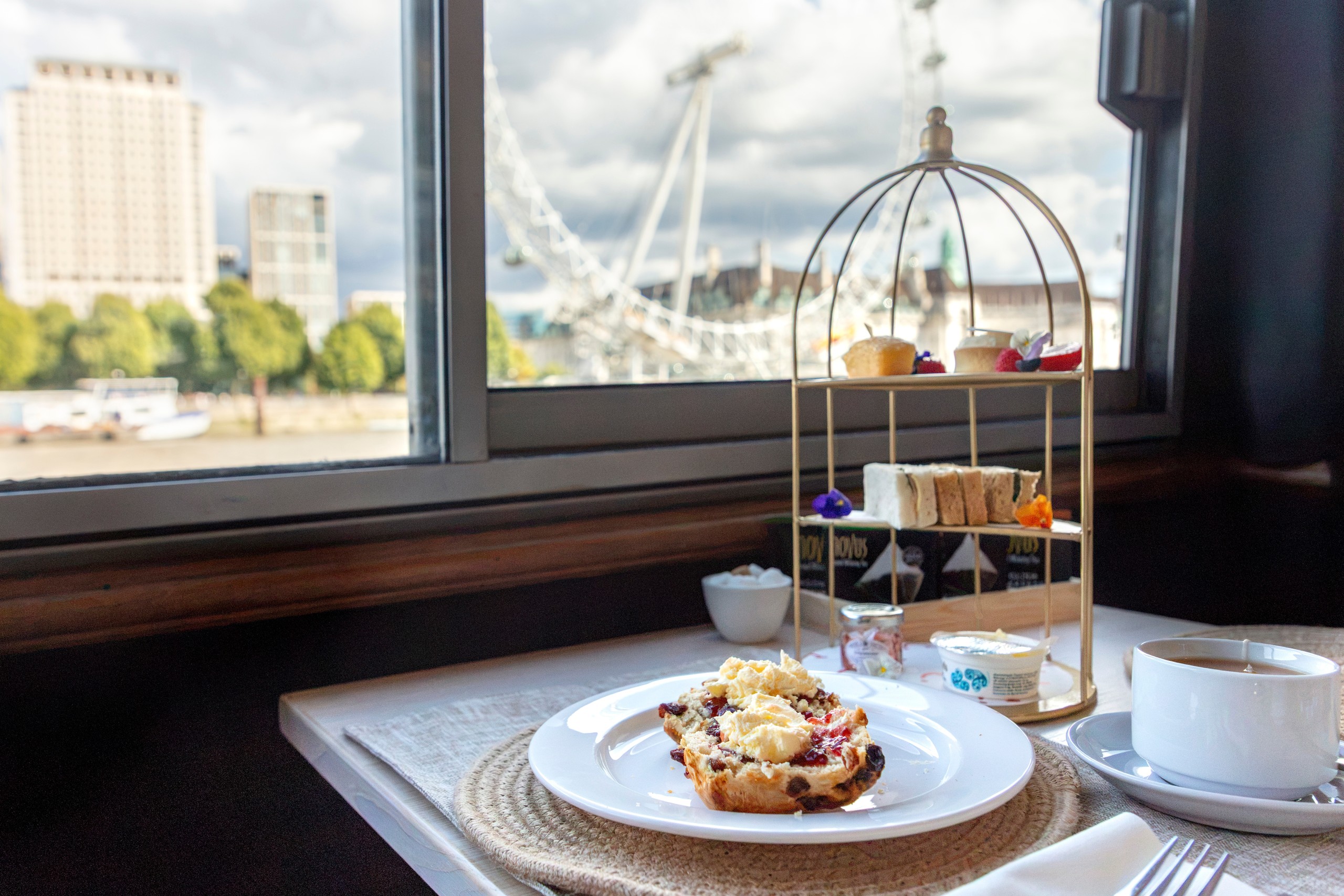 Tea set by window with London skyline, including Ferris wheel, visible outside.