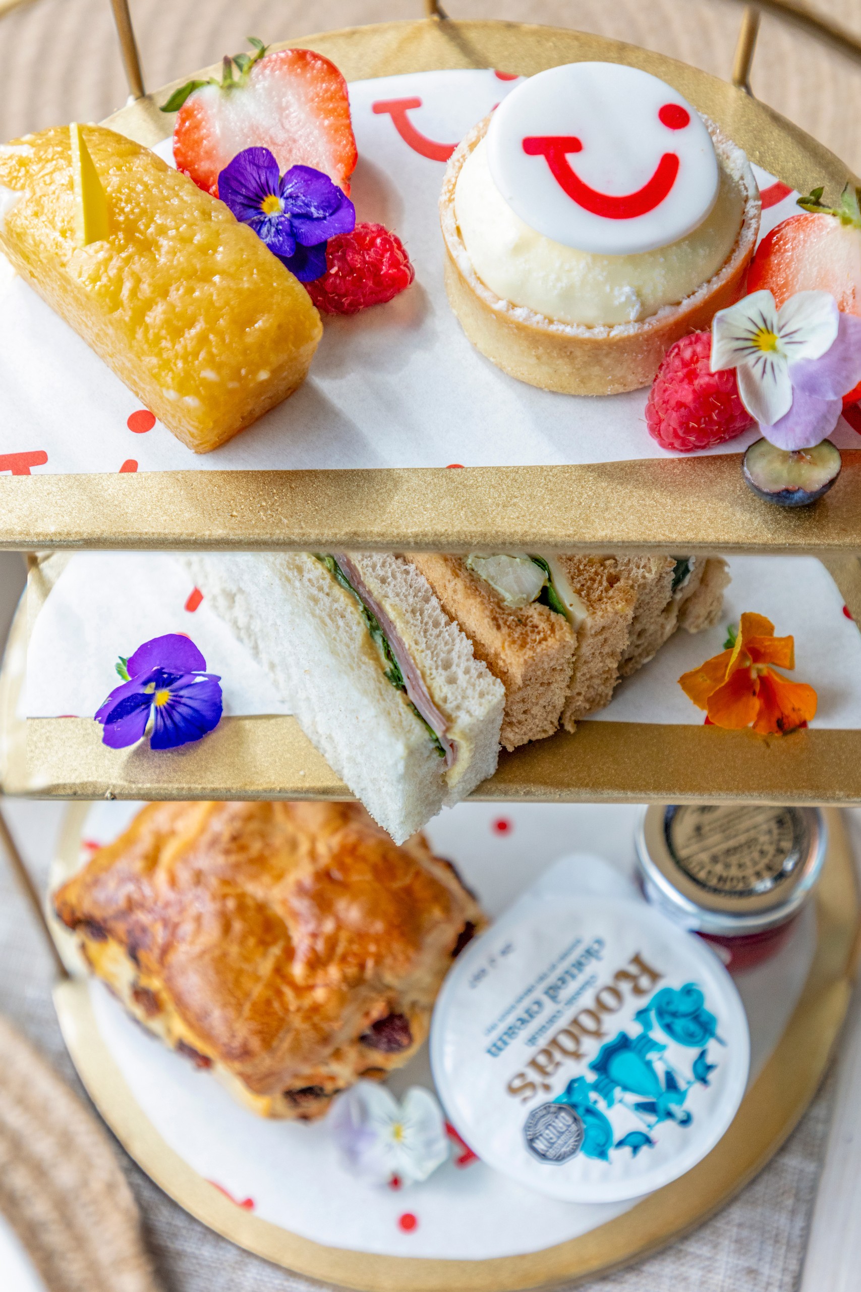 Three-tiered tray with pastries, sandwiches, and fruit.