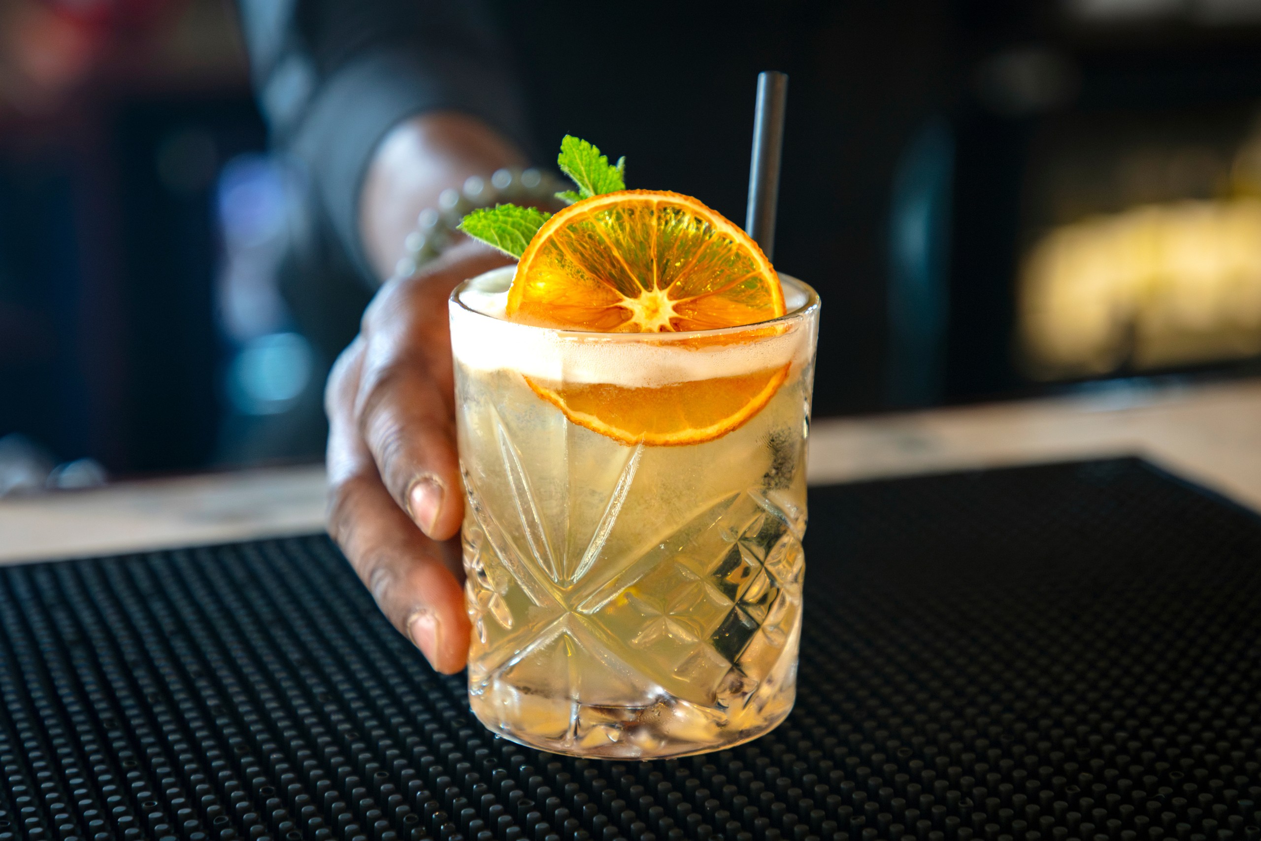 Hand serving cocktail with orange slice and mint in a glass