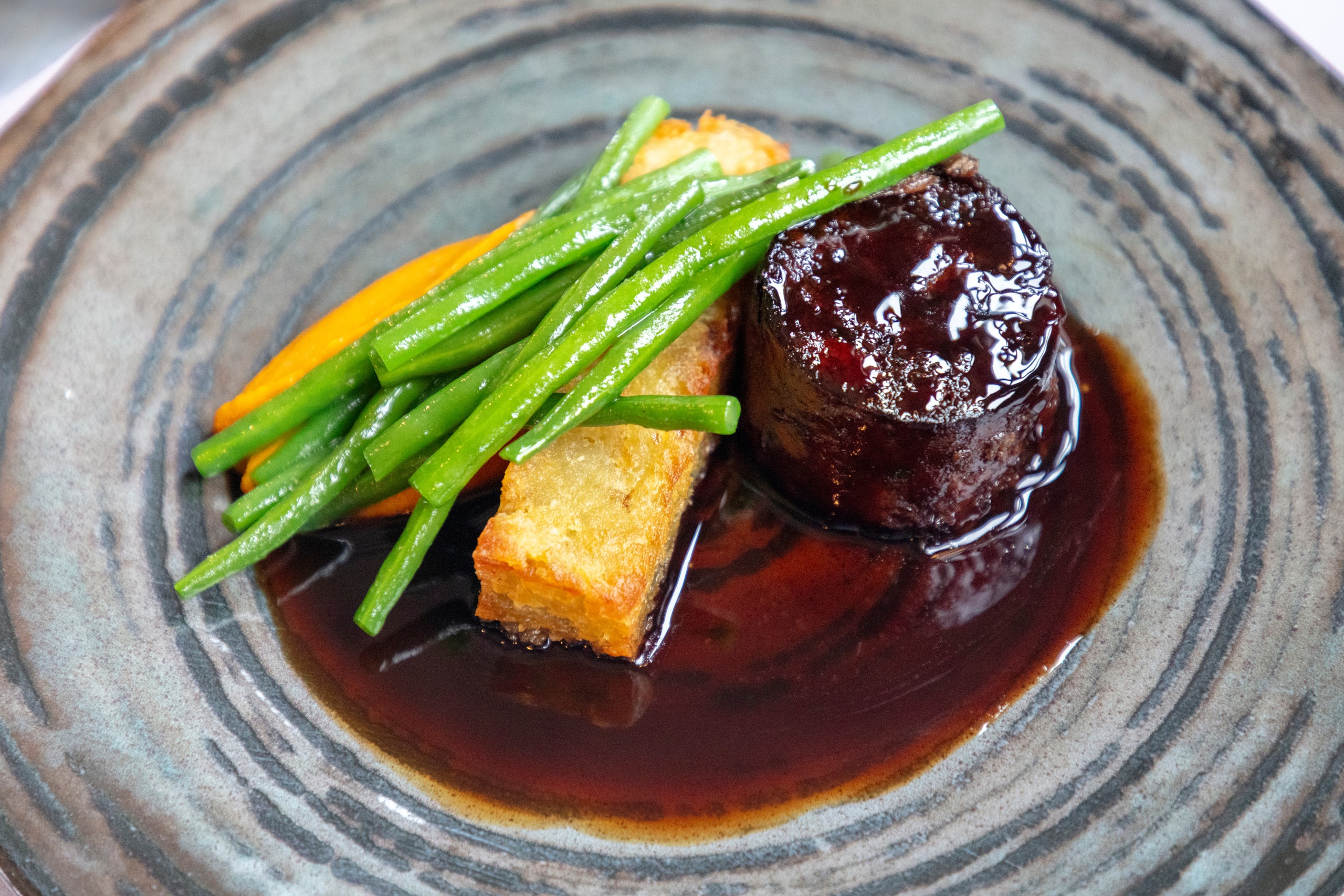 Plated gourmet dish with meat, green beans, potato, and sauce.