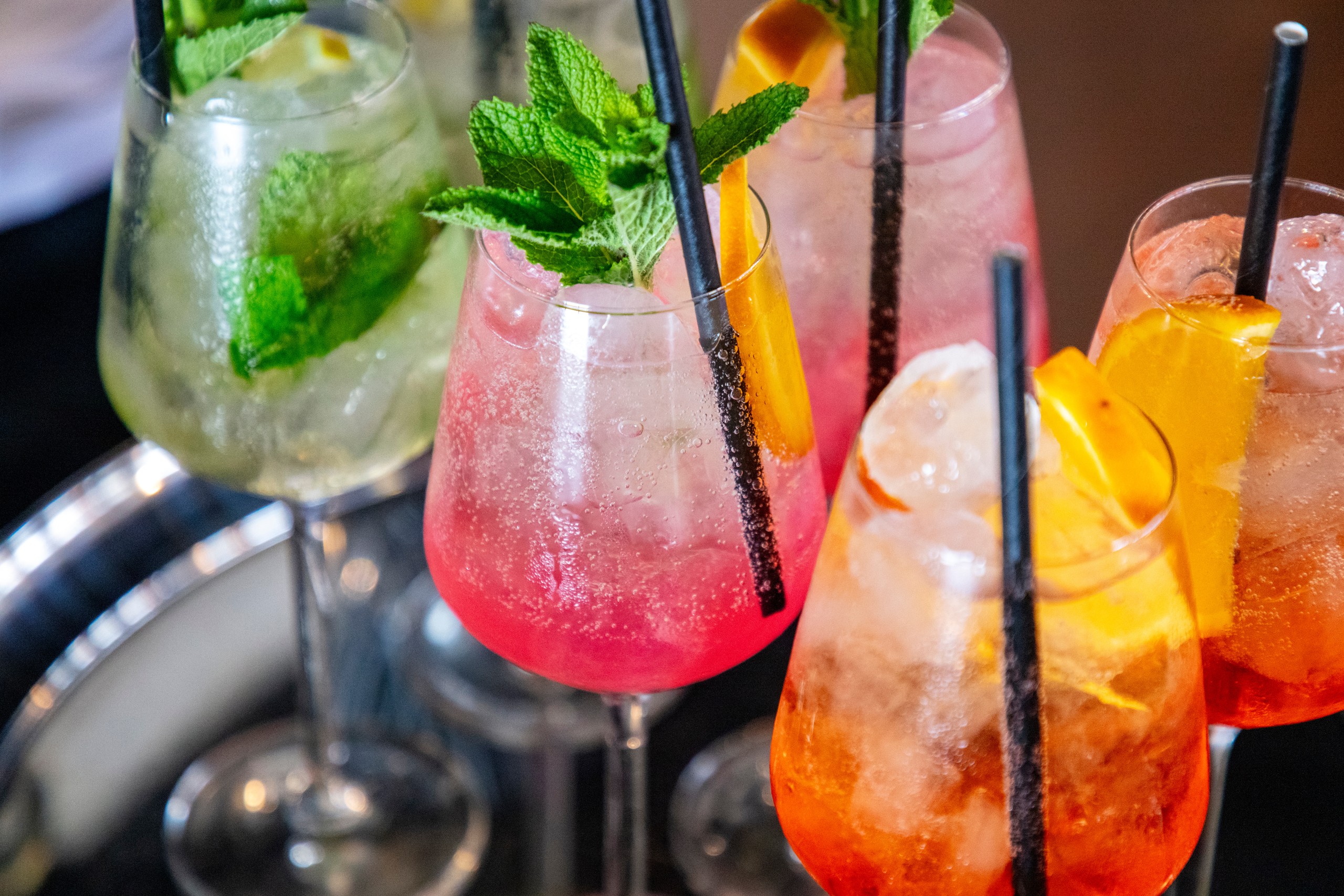 Colorful cocktails with mint and fruit garnishes in glasses with straws.
