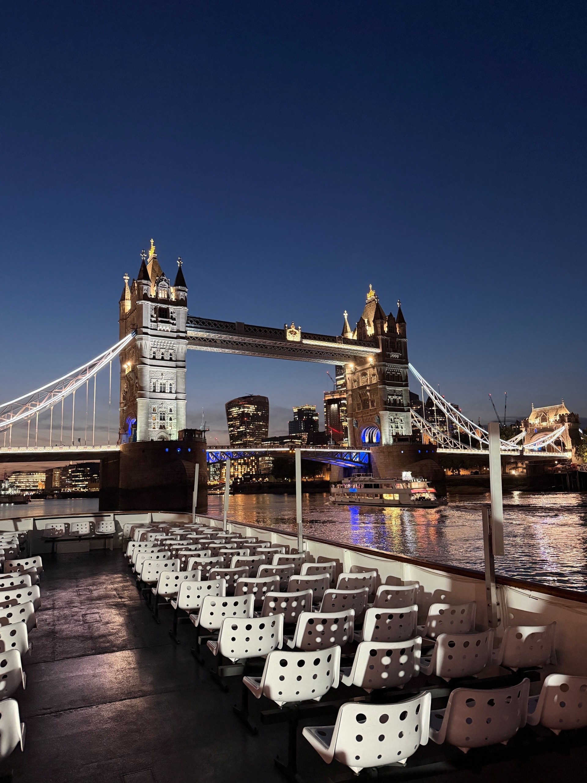 Tower Bridge at night with empty boat deck and city lights.
