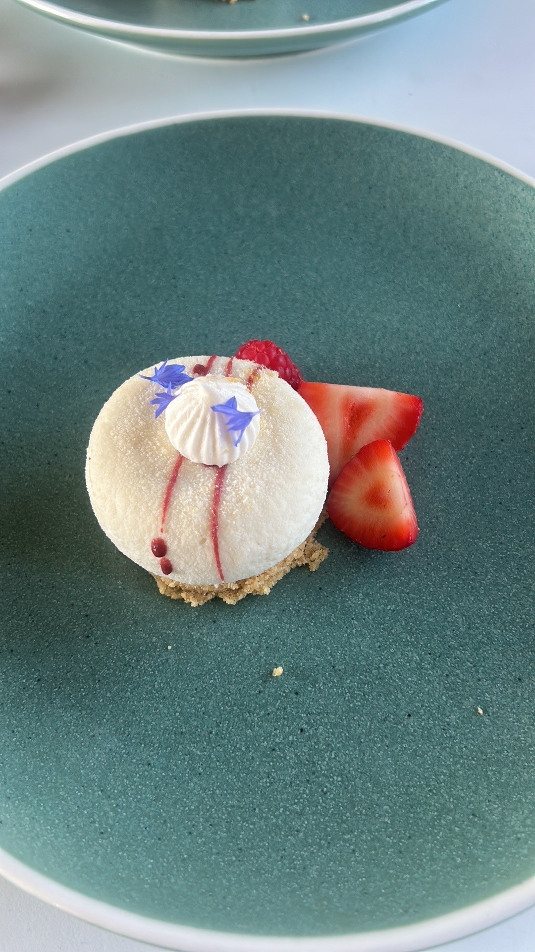 Elegant dessert with cream, red sauce, and strawberries on green plate.
