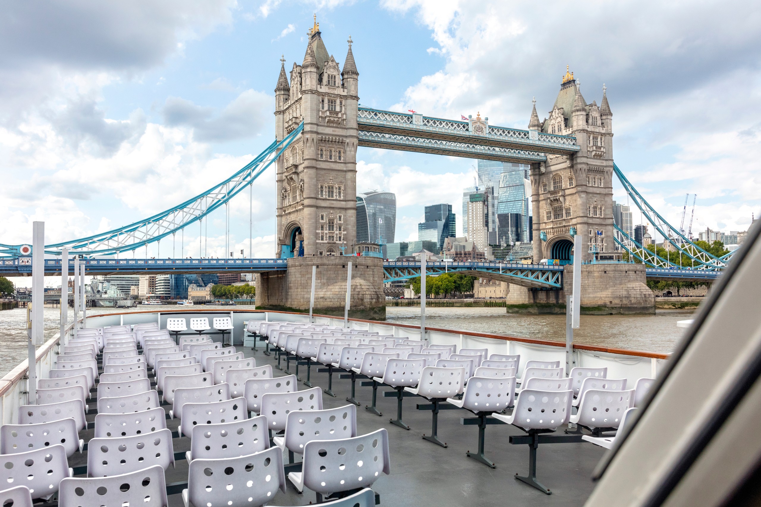 Empty boat seats facing Tower Bridge and city skyscrapers.