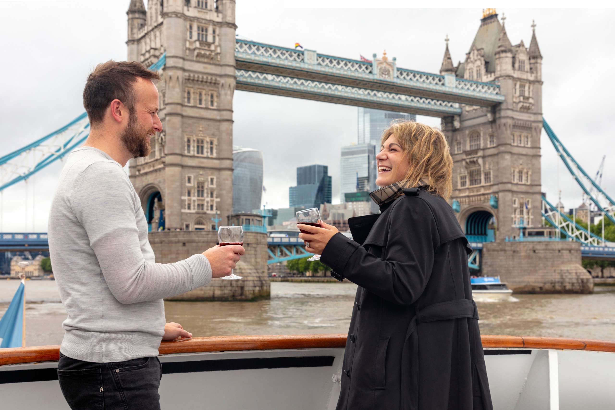 Two people enjoying drinks on a boat near Tower Bridge in London.