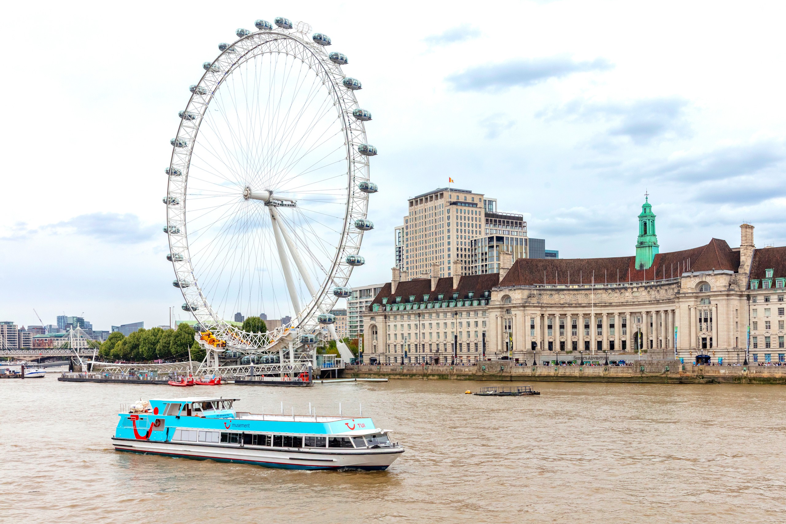 Boat on Thames River near London Eye Ferris wheel and historic buildings.