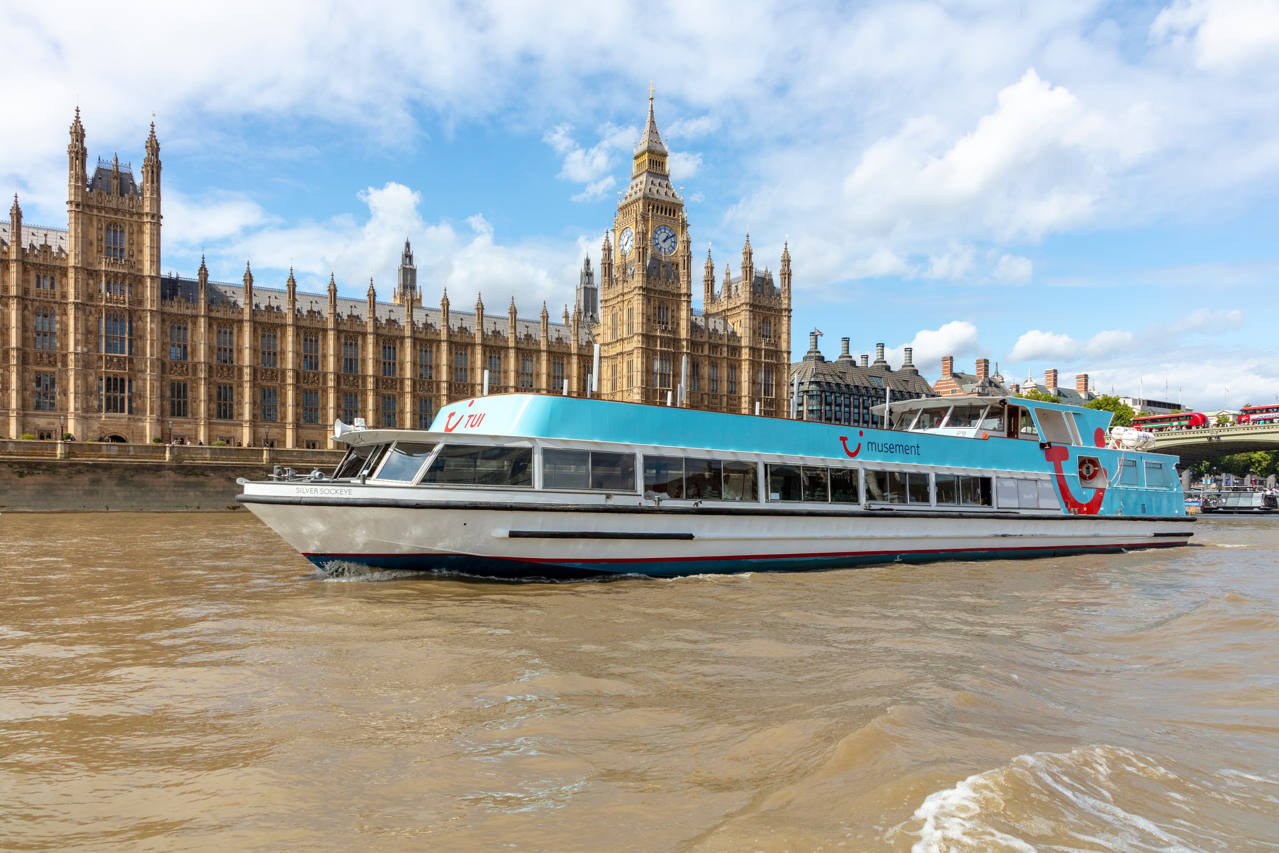 Riverboat passes Houses of Parliament on a sunny day.