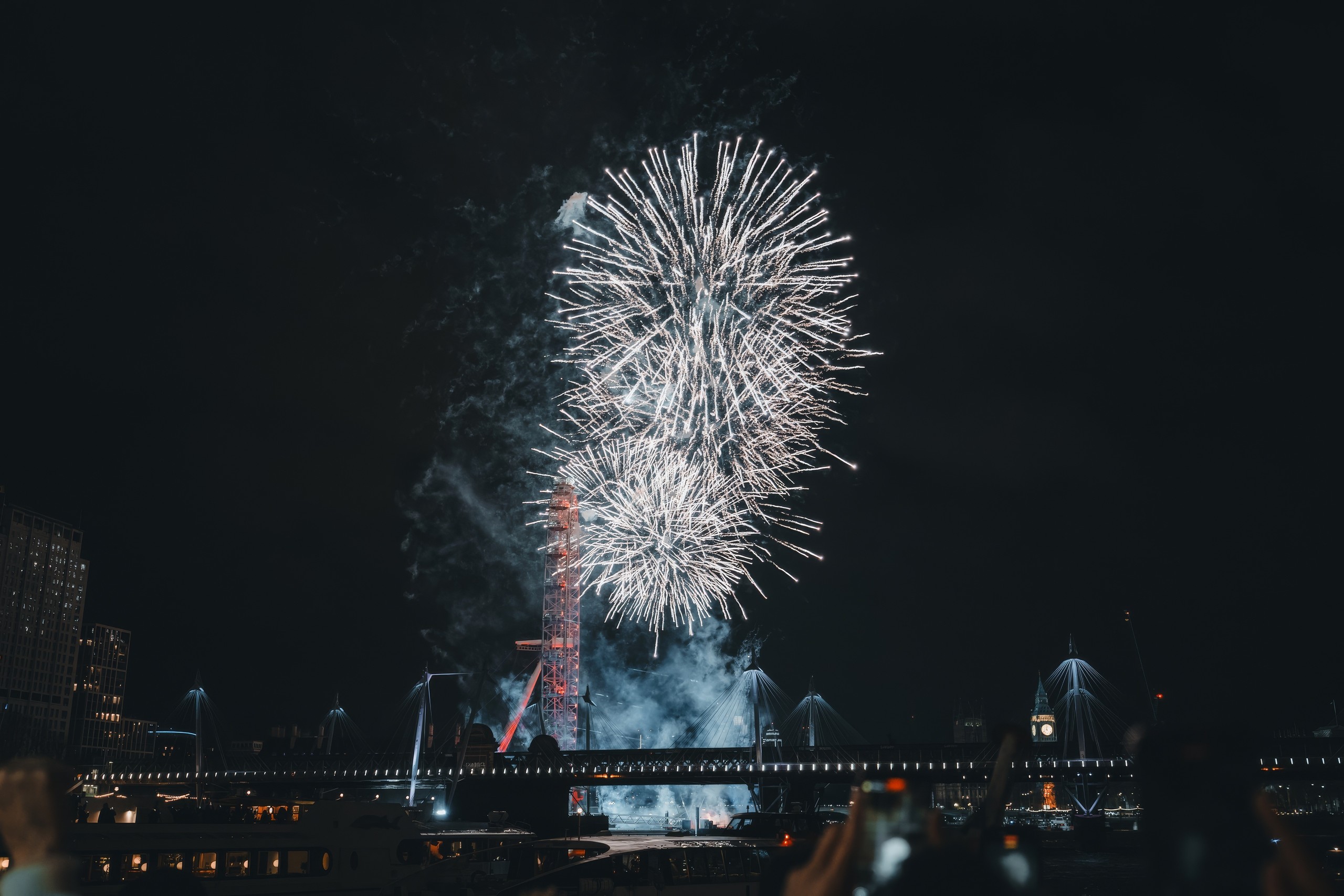Bright white fireworks over a cityscape at night with a Ferris wheel.