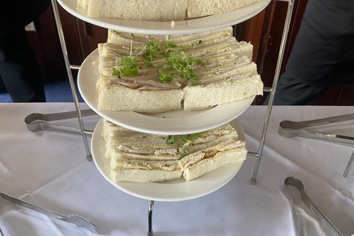 Tiered platter with roast chicken tarragon mayonnaise sandwiches, garnished with greens.