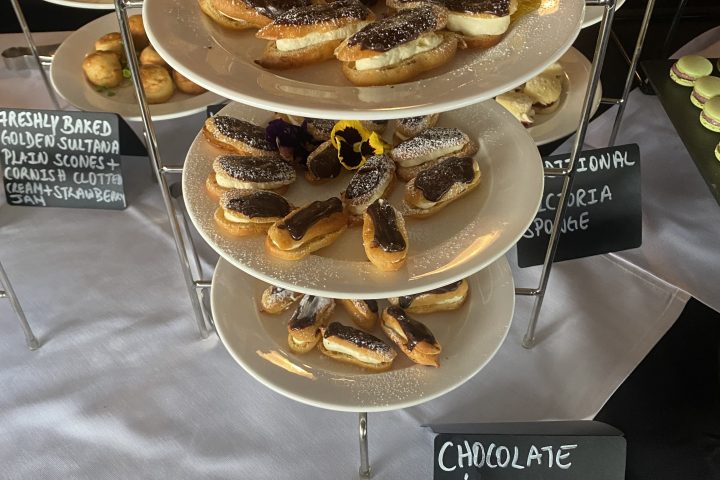 Three-tier stand with chocolate eclairs, scones, and sweets on a table.