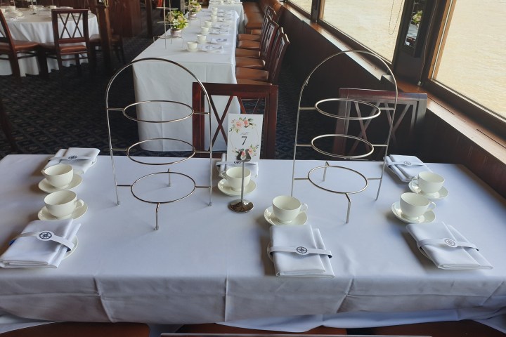 Table set for afternoon tea with cups, saucers, napkins, and tiered cake stands.