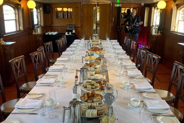 Elegant dining table with white cloth, set for a meal; man playing guitar in the background.
