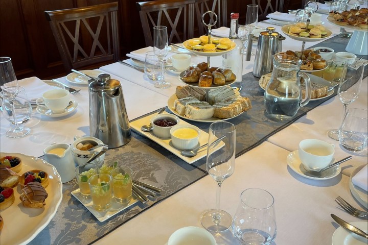 Elegant dining table set with pastries, sandwiches, drinks, and tea in a wood-paneled room with river view.