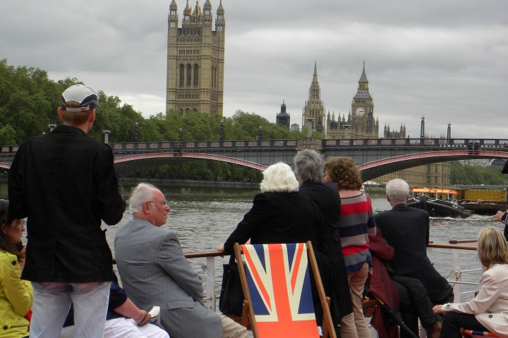 People on a boat with Parliament in the background, one chair with UK flag design.