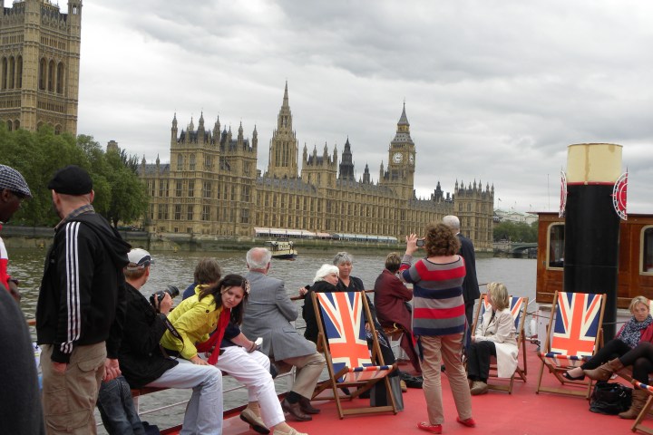 Tourists on a boat with Union Jack chairs, overlooking the Houses of Parliament, London.