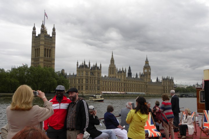 Tourists on a boat near the Houses of Parliament in London, cloudy sky above.