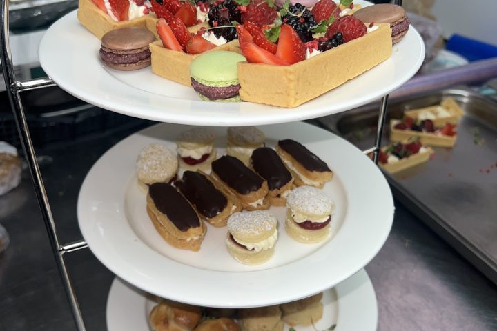 Three-tier tray with assorted pastries, macarons, and desserts on stainless steel counter.