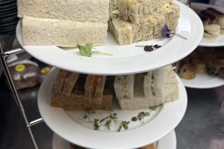 Three-tier stand with assorted sandwiches and pastries on plates.