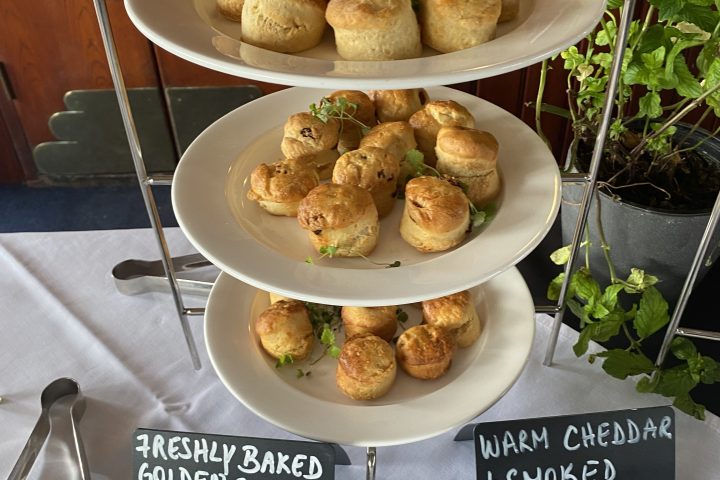 Three-tiered tray with assorted scones, two labeled signs, on a white tablecloth.
