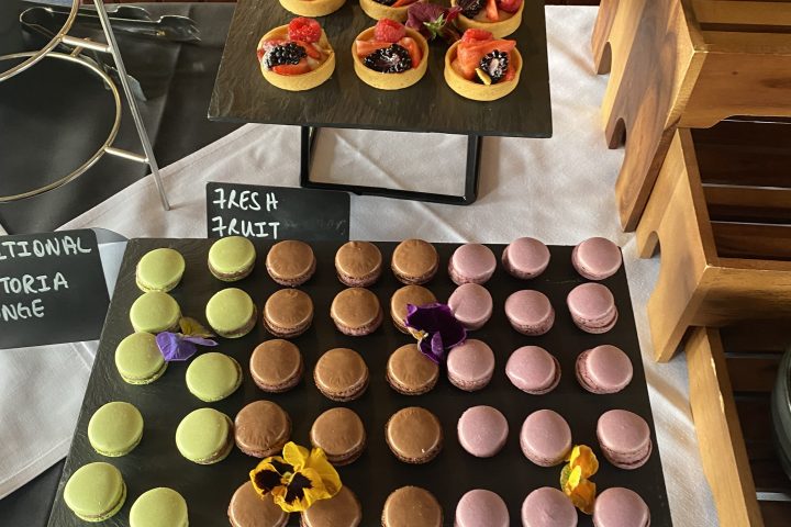 Display of assorted fruit tarts and colorful macarons on black trays.