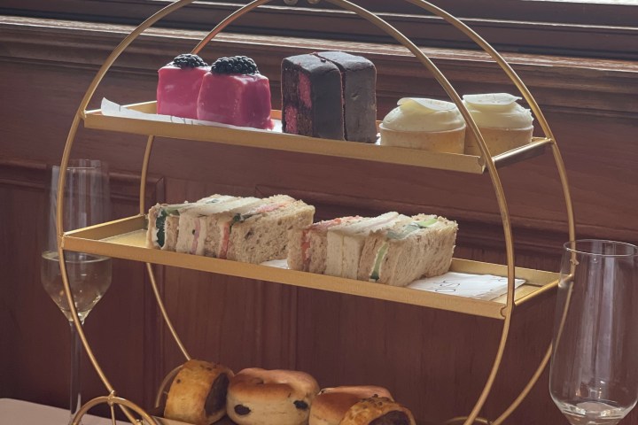Three-tiered stand with pastries and sandwiches near a window with view of water.