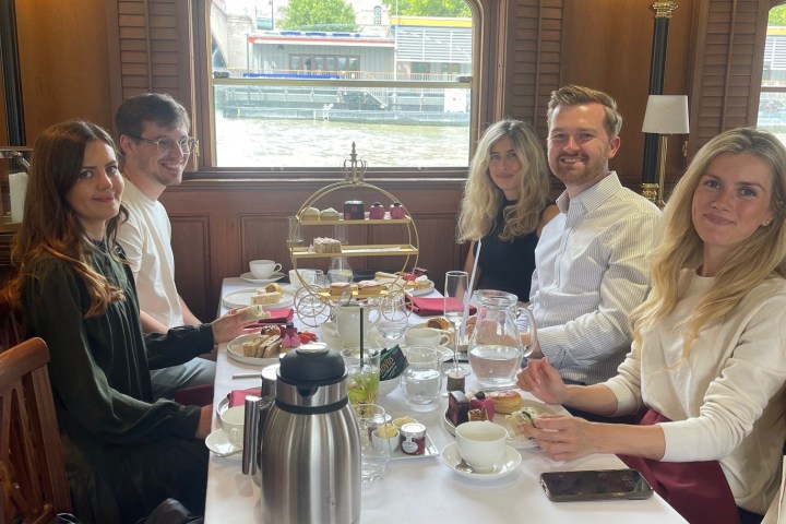 Five people sitting at a dining table with afternoon tea setup on a boat.