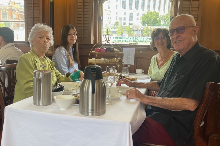 Four people sitting at a dining table inside a wood-paneled room with a window.