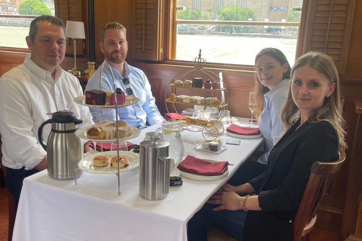 Four people having afternoon tea on a boat, with scones and pastries on the table.