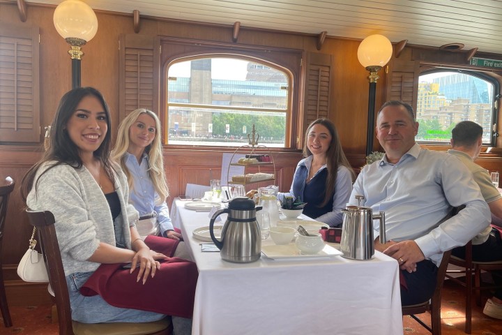 Four people seated at a restaurant table set for tea, with cityscape visible through the window.