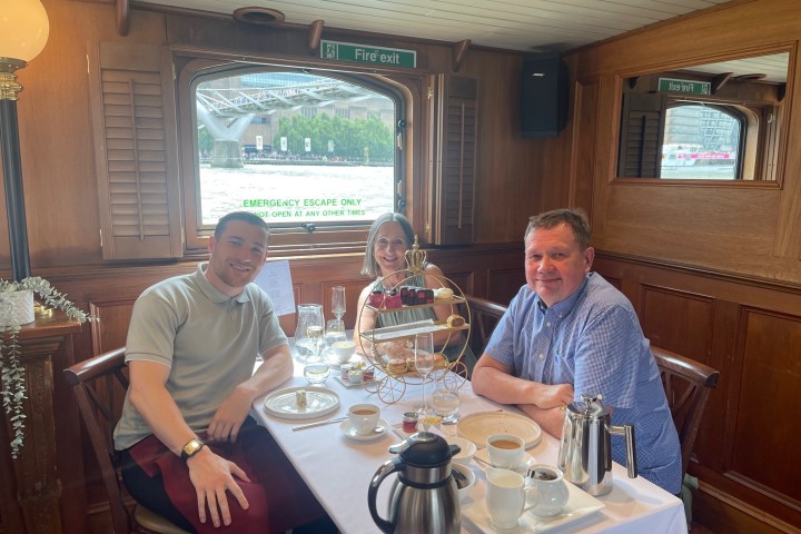 Three people seated at a table with afternoon tea on a boat.