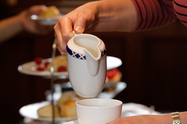 Person pouring cream into a teacup at a tea party.