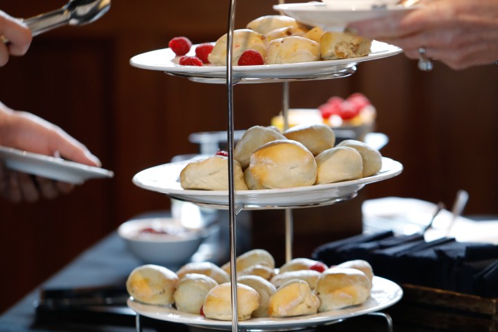 Three-tiered stand with scones and raspberries, hands with teacup and tongs.