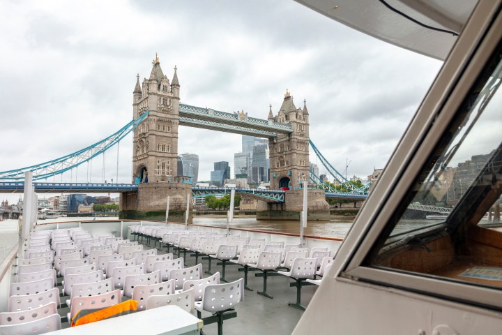 View of Tower Bridge from a boat, with empty seats and cloudy sky.