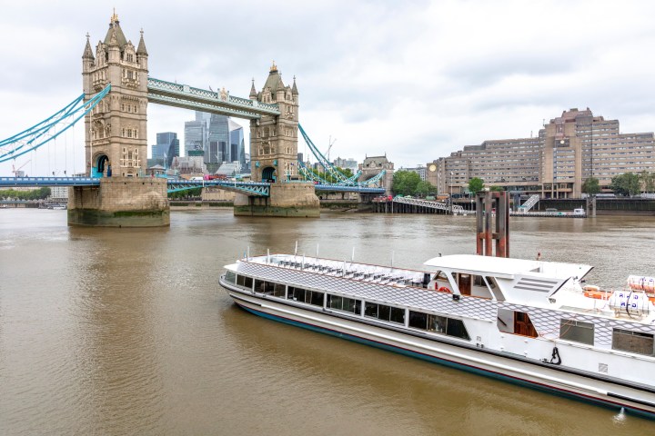 Boat on Thames River with Tower Bridge and cityscape in background.