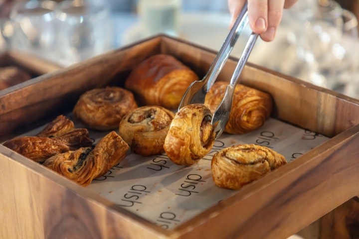 Hand using tongs to pick up pastries from a wooden box.